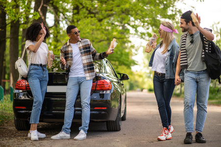 Group of riends having lunch and discussing something while standing near the car in the forestの写真素材