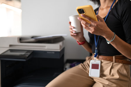 Woman sitting in the office with a phone and cup with coffee in handsの写真素材