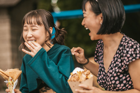 Cute young girls enjoying street food and looking entertainedの写真素材