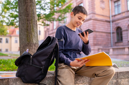 Cheerful schoolboy using his mobile phone outsideの写真素材