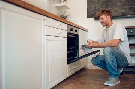 Ginger man in casual clothes near the oven in the kitchenの写真素材