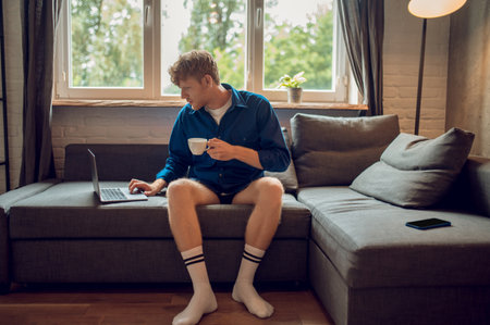 Young ginger man with a coffee mug in hand checking his emailの写真素材