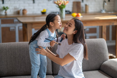 Child with cosmetic tools kissing her happy female parentの写真素材