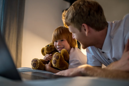 Father and son lying on bed and watching something on internet before going to sleepの写真素材