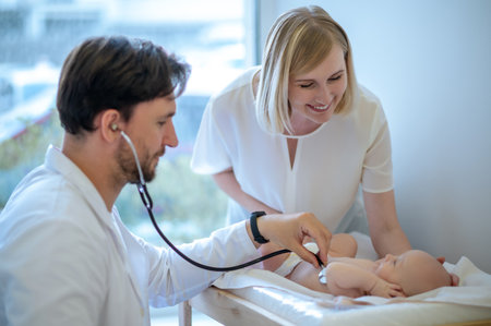 Mom smiling to a baby while pediatrcician listening to babys heartの写真素材