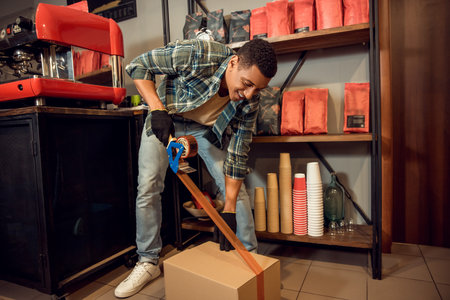 Joyful young cafe worker taping a closed cartonの写真素材