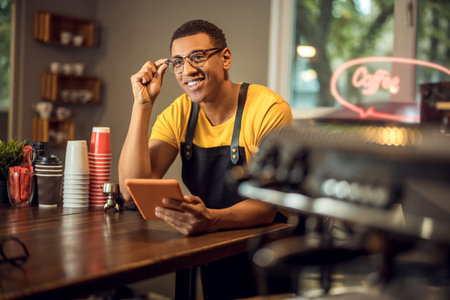 Joyous coffee house worker with a gadget in the workplaceの写真素材