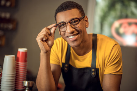 Joyful barista wearing an apron and eyeglasses at workの写真素材