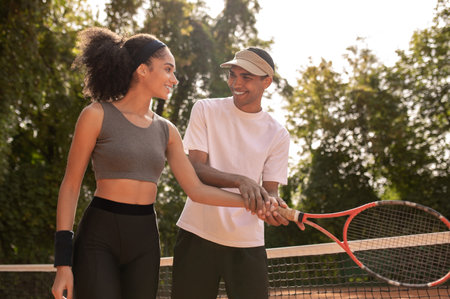 Young male coach teaching a curly-haired girl to play tennisの写真素材