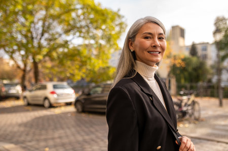 Smiling pretty woman in a black coat in the city streetの写真素材