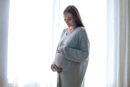 Long-haired pregnant woman standing near the window