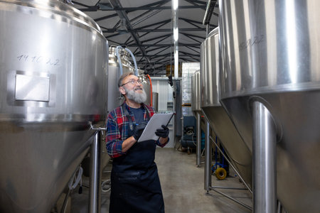 Man in plaid shirt checnking the tanks with beer at the breweryの写真素材