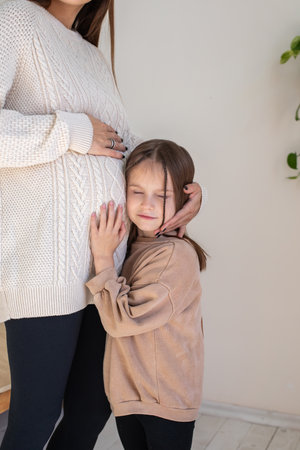 Cute little girl listening to babys moves in pregnant moms bellyの写真素材