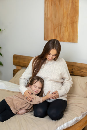 Pregnant young woman and a little girl on the bed looking peaceful