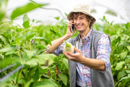 Pleased vegetable grower talking on the smartphone in the hothouseの写真素材