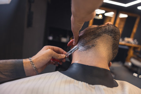 Barber with tattoed arm carefully shaving the clientの写真素材