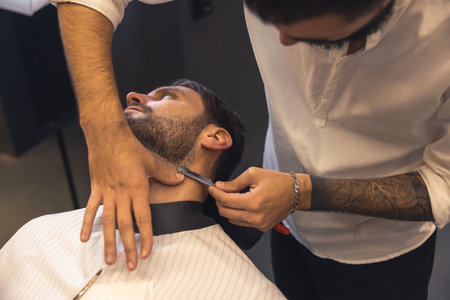 Barber with tattoed arm carefully shaving the clientの写真素材