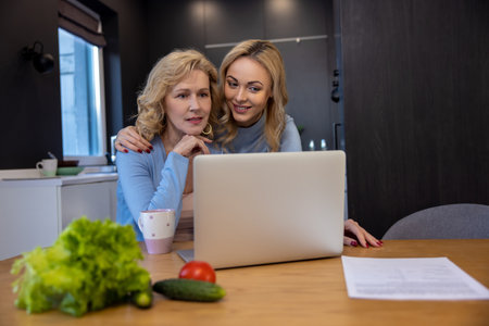 Two women using the portable computer in the kitchenの写真素材
