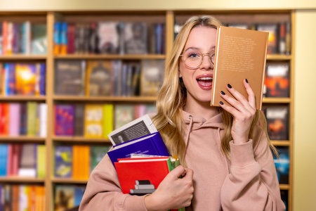 Pretty blonde woman standing with books in libraryの写真素材