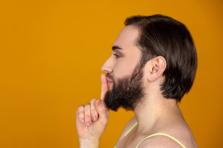 Side view of bearded transsexual person holding finger near lips making silence gesture keeps secretの写真素材