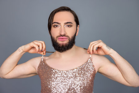 Transsexual person wearing shiny tank top looking at camera touching his fashionable clothingの写真素材