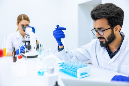 Team of scientists examining sample, using microscope and chemical liquids in flask in modern lab