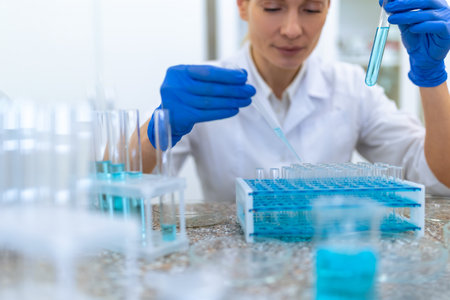 Unrecognizable female scientist or doctor working with liquid in flask, using pipette
