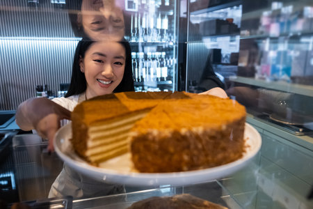 Smiling coffeehouse employee reaching for a delicious cakeの写真素材