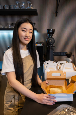 Pleased cafe worker preparing a slice of cake for takeaway