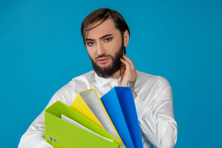 Elegant transsexual guy manager with beard holding multicolored paper folders doing office work