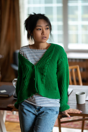 Asian girl in green shirt at home looking thoughtfulの写真素材