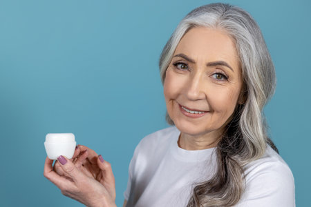 Long-haired senior good-looking woman holding a jar of face creamの写真素材