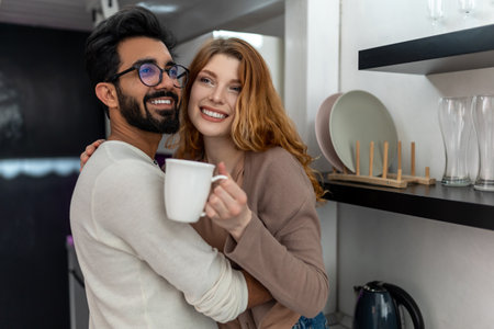 Woman drinking coffee with man and hugging while sitting on kitchen counter.の写真素材