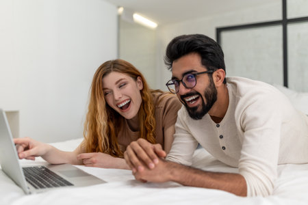 Man and woman spending time at home watching movie on laptop while laying on bed.