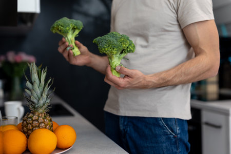 Man holding green fresh broccoli standing in modern kitchen at home.