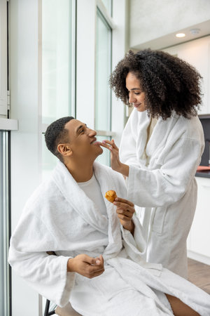 Young couple in white bath robes habing breakfast and looking happyの写真素材