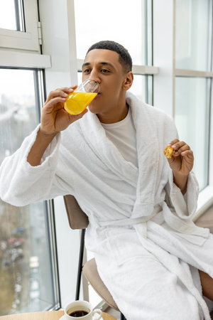 Good-looking young man in white robe having healthy breakfastの写真素材