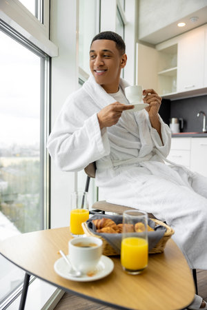 Good-looking young man in white robe having healthy breakfastの写真素材