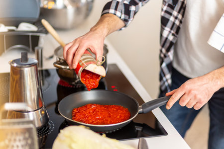 Man cooking at home kitchenn adding sauce to pan.の写真素材