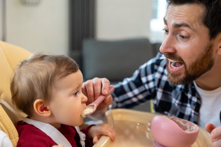 Baby eating her dinner with dad, father feeding toddler kid.