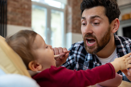 Father feeding his infant baby in home interior teaching toddler kid eating from spoon.の写真素材