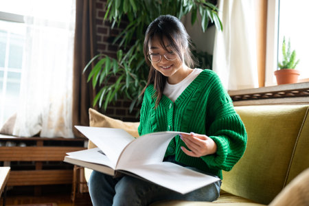 Young asian girl with a big book sitting on the sofaの写真素材