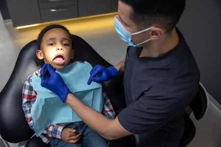 Dark-skinned boy looking scared while doctor checking his teeth