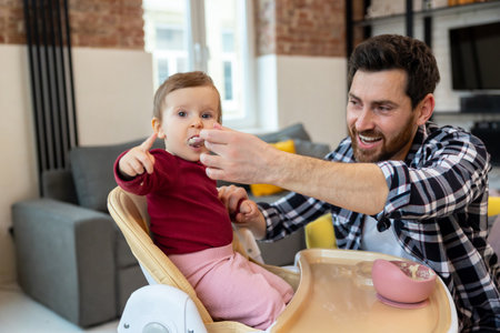 Bearded father feeding little baby daughter sitting in highchair with puree or porridge.の写真素材