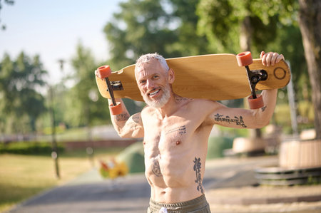 Smiling mature man holding longboard in a city park.の写真素材