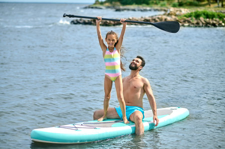 Dad and his daughter surfing paddleboarding, having happy time spending summer holiday in active wayの写真素材