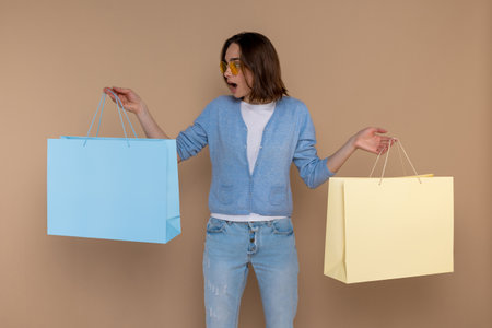 Amazed surprised shocked woman in casual clothing holding shopping bags in handsの写真素材