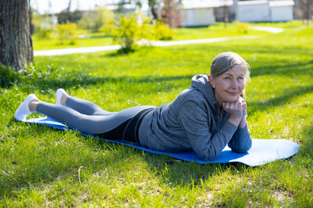 Mature woman in grey sportswera doing yoga in the parkの写真素材