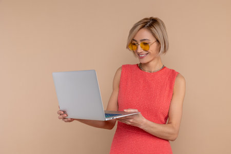 Happy woman in dress and sunglasses working online using laptopの写真素材
