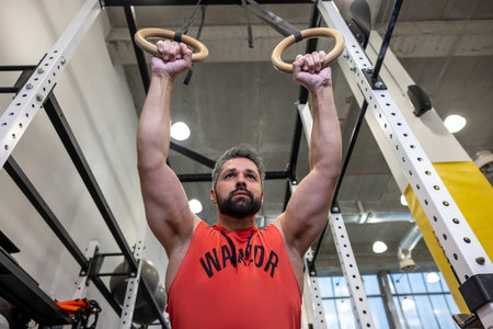Powerful man exercising with gymnastic rings at gym.